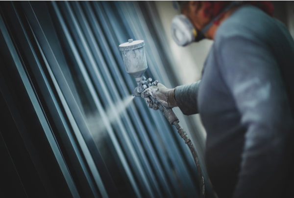 Man painting metal products with a spray gun